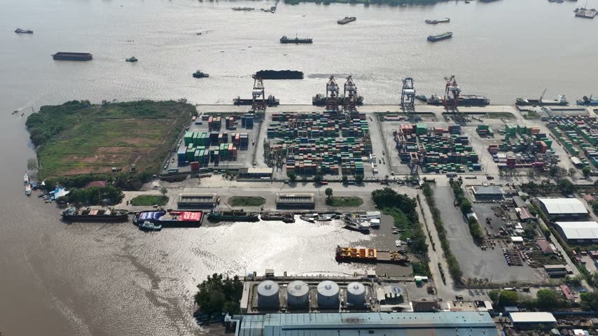 Busy industrial shipping port facility located on the riverbank during a sunny afternoon