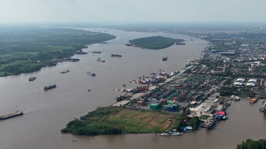 Barges and cargo ships navigate the wide Barito River near the busy port of Banjarmasin