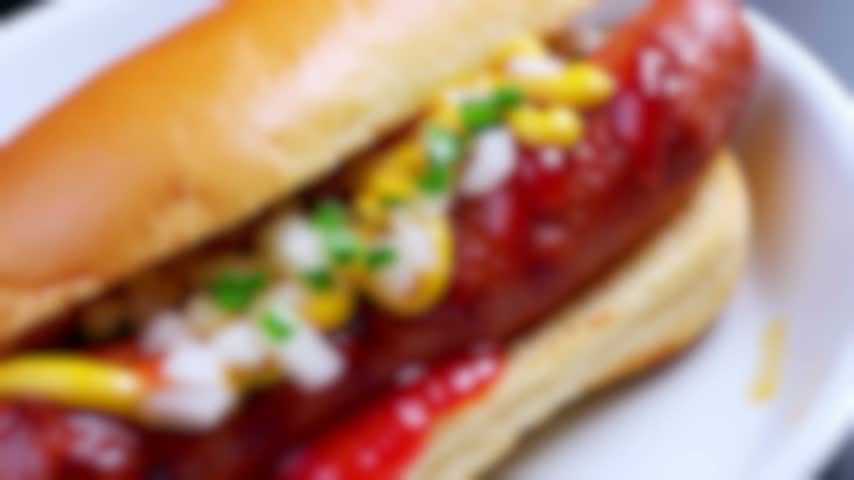 A close up shot of a delicious hot dog in a bun with mustard ketchup and chopped onions.