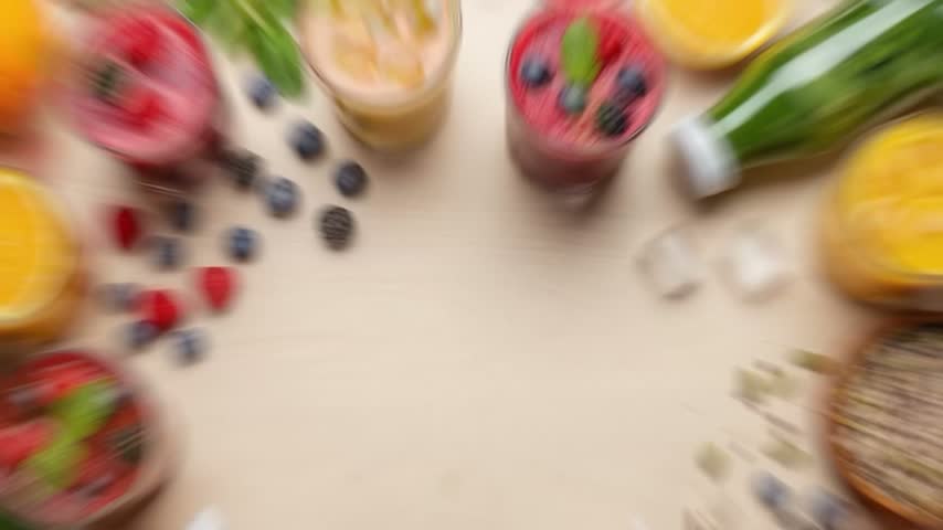 A top-down view of various colorful fruit smoothies and fresh ingredients like berries and oranges arranged on a light-colored table, creating a healthy and vibrant composition.