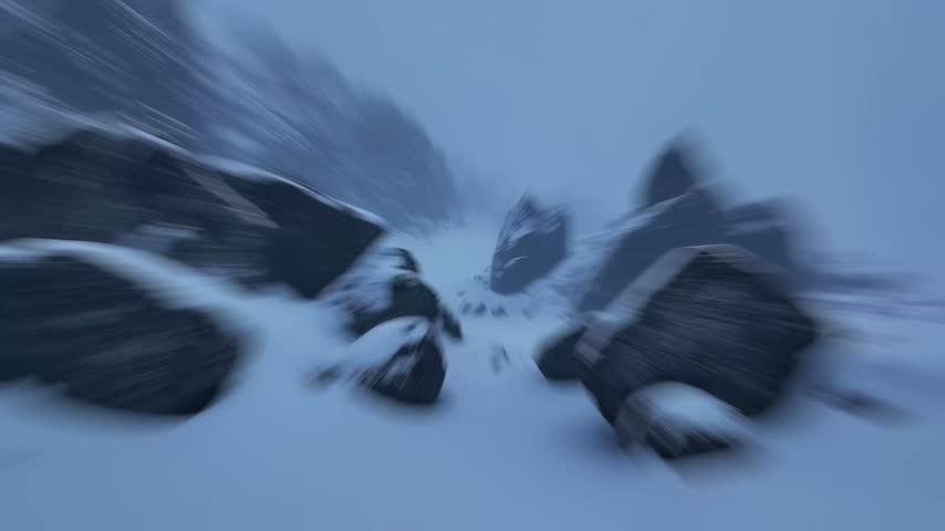 A blurry, atmospheric view of a snowy mountain path with large rocks and a dense fog.