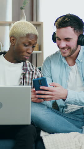 Portrait of cute joyful satisfied amorous 25-aged mixed race male lovers which relaxing on the sofa in cozy sitting room at daytime,african american boyfriend working on computer while another partner