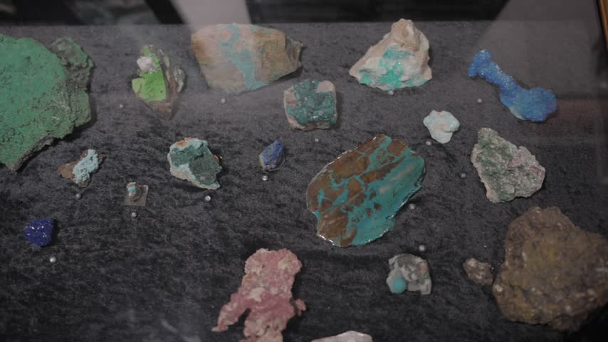 A clean, sharp shot focusing on a collection of vibrant, rare geological minerals and crystal specimens displayed inside a glass showcase with a solid black backdrop. Excellent for geology documentaries, educational science videos, jewelry design content, and projects highlighting natural crystals, earth science, and precious mineral stones.
