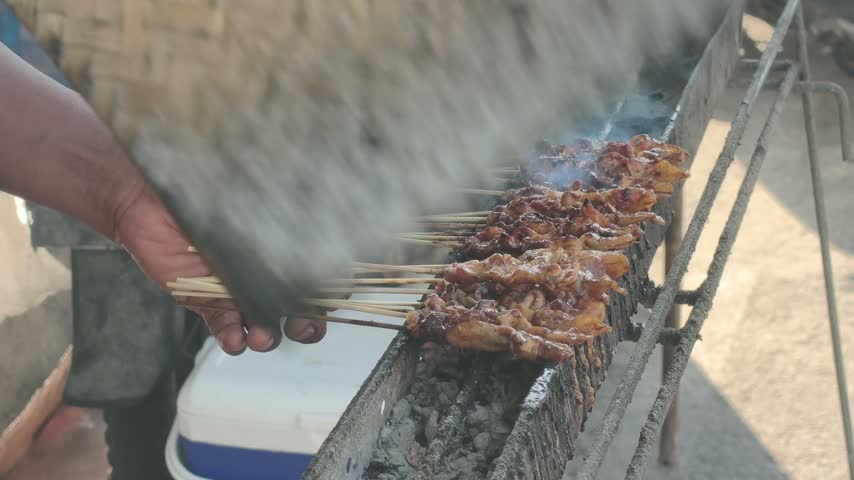 A chef grills Asian satay meat on a barbecue grill—chicken and goat satay—a type of street food.