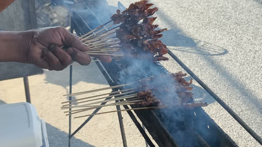 A chef grills Asian satay meat on a barbecue grill—chicken and goat satay—a type of street food.