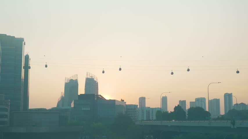 Singapore city skyline silhouetted against a vibrant sunset with cable cars passing above.