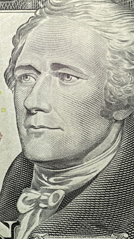 Alexander Hamilton portrait under green scan. Portrait on ten dollar bill glows as green security scan moves across banknote. Alexander Hamilton remains visible while light sweep highlights crisp currency texture.