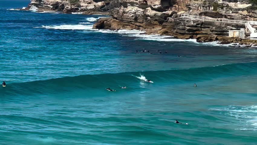 Surfer riding big ocean wave near rocky coast in turquoise sea water
