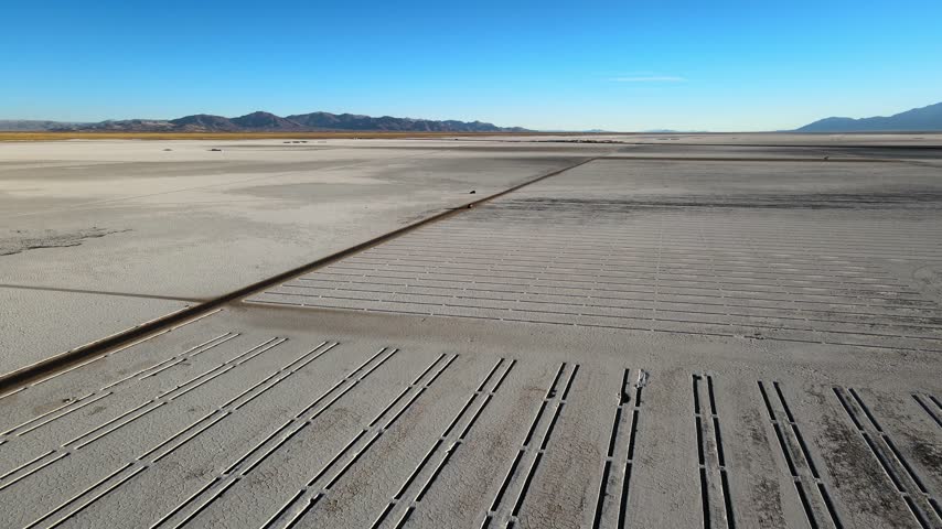 Gridded evaporation channels cut across the Salinas Grandes salt flat with distant Andes mountains under clear blue sky, useful for lithium mining, environment, or climate stories.