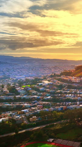 Sunset view of suburban neighborhood, San Francisco, California. High angle perspective of residential housing sprawl, rolling hills and warm golden hour sunlight under cloudy sky. Vertical video.