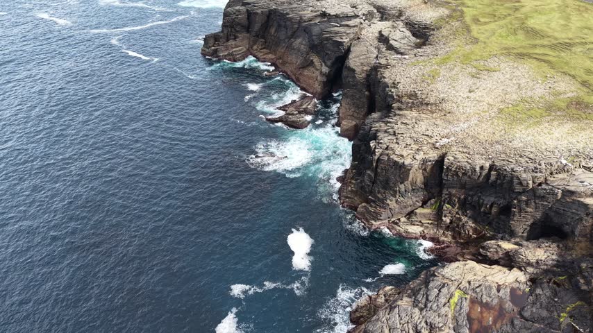 Aerial drone footage revealing dramatic layered sea cliffs and a rugged rocky shoreline near Eagle Island Lighthouse and Aghleam on the Mullet Peninsula, County Mayo, Ireland. Dark rock formations, deep Atlantic water and turquoise waves breaking around the cliffs create a striking Wild Atlantic Way coastal landscape.
