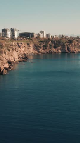 Aerial shot of rocky cliffs along the Mediterranean coast in Antalya with city buildings above.