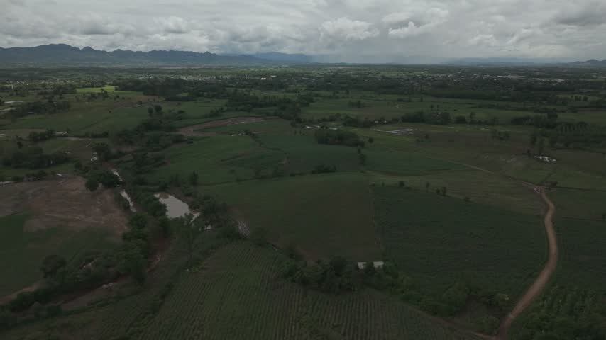 Drone footage capturing a hillside farming community with lush hills and overcast weather.