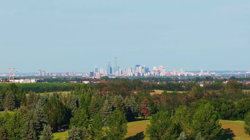 Distant view of the downtown Edmonton skyline rising above dense green trees and river valley foliage in Alberta, Canada