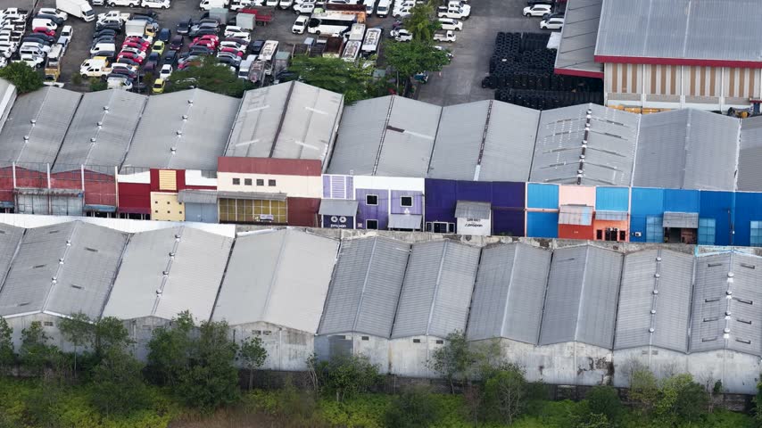 Rows of industrial warehouse buildings with cars parked in a large lot during the bright daytime