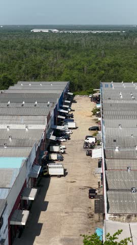Rows of industrial buildings and warehouses located near a vast green forest landscape at midday