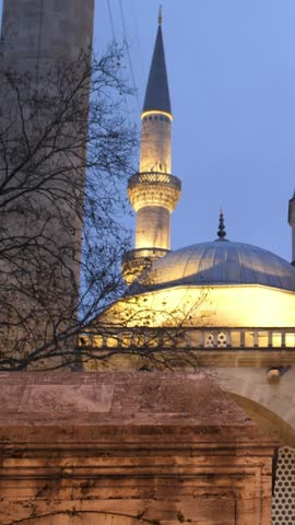 Low-angle tilt-up shot of the illuminated Suleymaniye Mosque at dusk in Istanbul, Turkey, with birds flying near its domes.