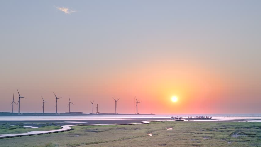 Scenic sunset view over Gaomei Wetland in Taichung, Taiwan, featuring wind turbines, wooden boardwalks, and visitors enjoying the evening scenery.