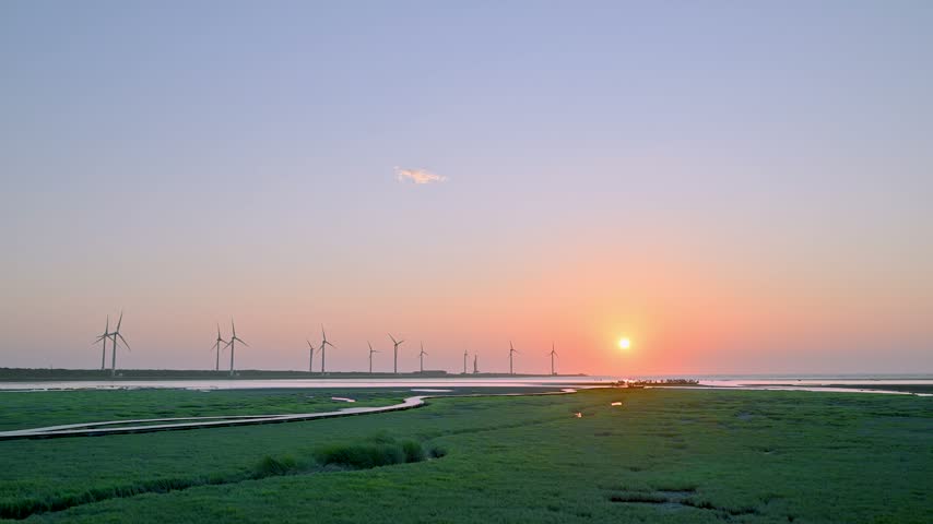 A scenic sunset over Gaomei Wetland in Taichung, Taiwan, featuring wind turbines and green marshland.