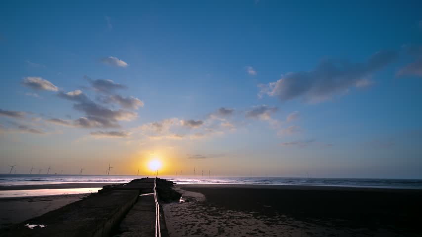 Scenic view of sunset over the ocean at the beach in Miaoli, Taiwan, featuring offshore wind turbines and a concrete pier in the foreground.