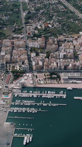 An aerial view of a coastal city harbor filled with docked boats and yachts. The footage captures the urban port area and surrounding blue water.
