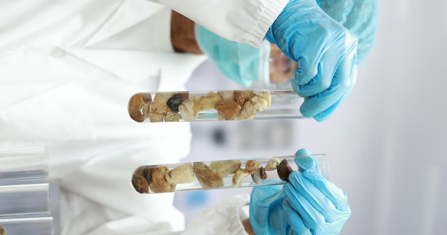 Scientist in protective gloves holding test tubes with soil and rock samples in a bright laboratory, representing research, analysis, and environmental study.