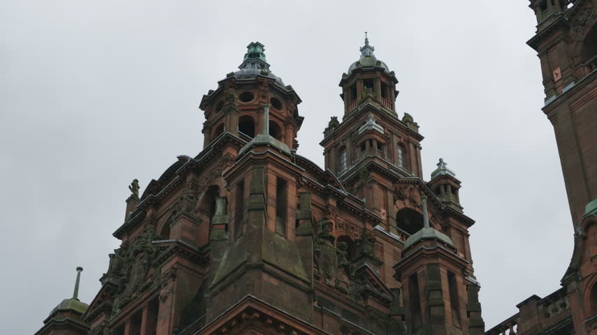 Tight low-angle shot highlights the ornate towers and roof architecture of Kelvingrove Art Gallery and Museum under an overcast sky.