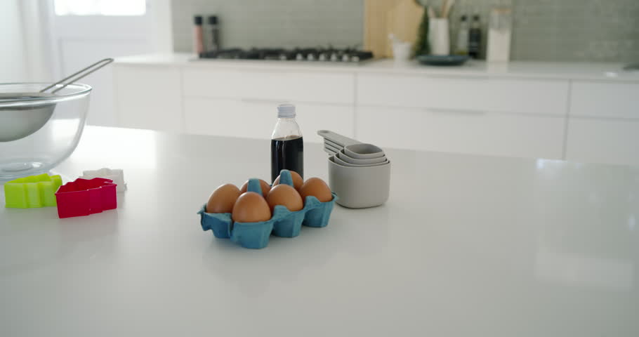 Camera is panning left, revealing bowl with sieve and milk carafe on island for baking. Kitchen, baking, countertop, utensils, ingredients, measuring, cookie