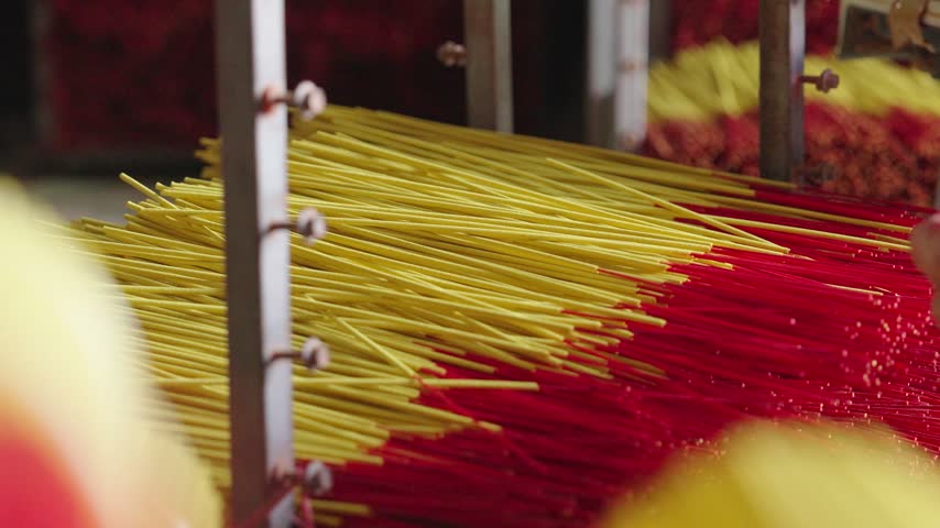 Worker gathers and ties finished yellow and red incense sticks into a compact bundle after drying. Close-up view shows the manual bundling stage used to organize incense before final packaging.
