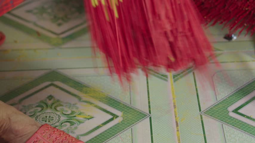 Worker gathers and ties finished yellow and red incense sticks into a compact bundle after drying. Close-up view shows the manual bundling stage used to organize incense before final packaging.