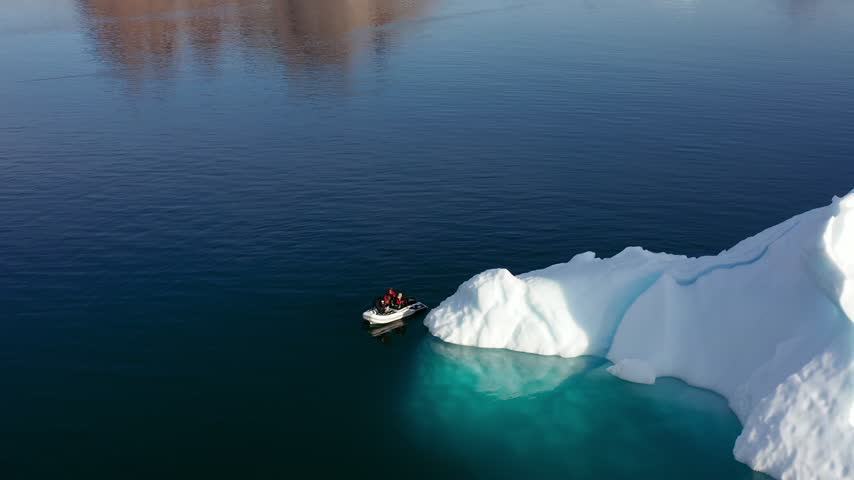 Motorised Rubber Boat Travelling Among Floating Icebergs In The Remote Arctic Waters Of East Greenland. Aerial Drone Shot