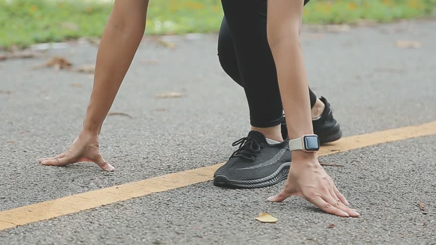 Close up low angle motion shot of a female runner starting race. Athletic woman in black leggings and sneakers on a paved path.