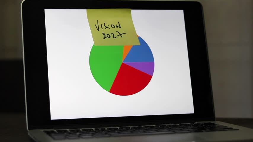 A horizontal shot of a man sticking sticky notes with his goals for the year on a computer screen