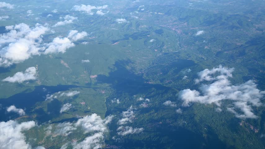 Aerial view of green hills and scattered clouds.