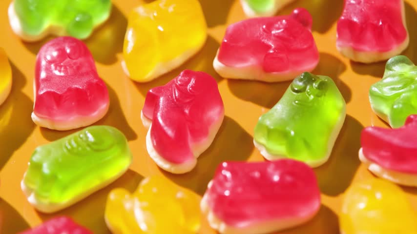 colorful gummy candy ghosts of yellow, red and green colors top view on yellow background, halloween background