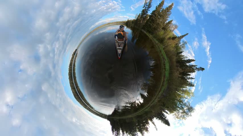 Wide angle globe like view of person paddling a canoe on a calm lake in a northern forest