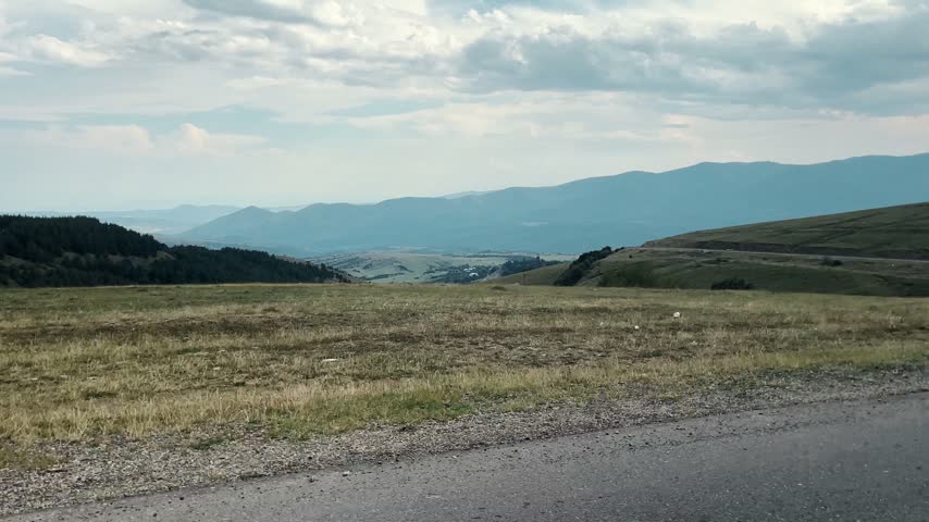 View from a moving car while driving through a mountain pass in Georgia. Scenic highland road and distant valleys represent travel, road trip and adventure.
