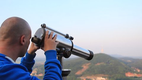 male in blue cardigan watches the environment with a telescope