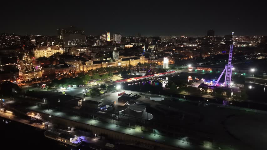 Nocturnal aerial drone orbit shot moving rightward over the Old Port, showcasing the illuminated Grande Roue wheel and Bonsecours Market in Montreal at night
