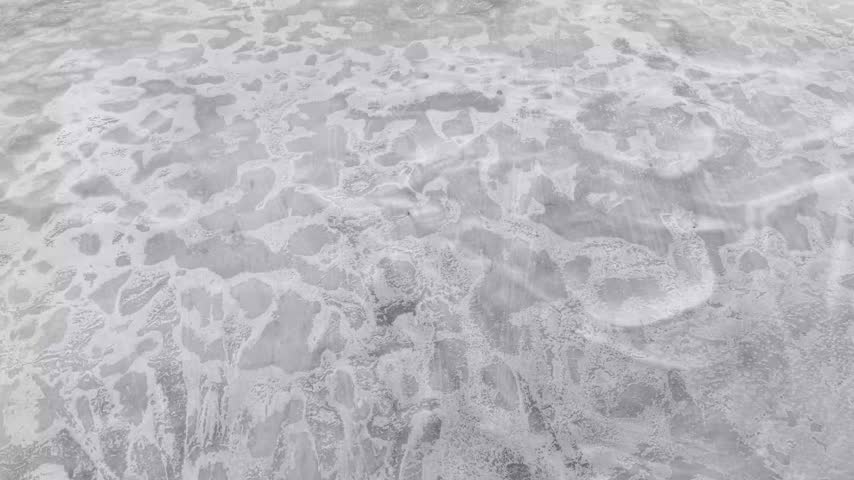Smooth aerial drone flyover tilting up from textured ice to reveal an expansive frozen lake surrounded by wilderness forest in winter.