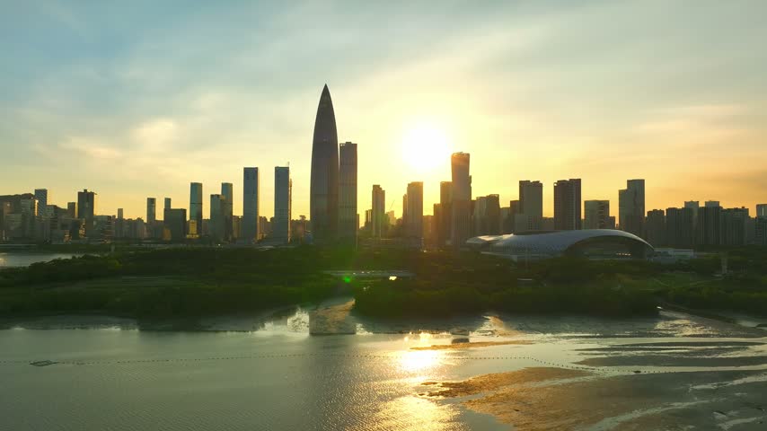 Aerial view of sunlit bay and exposed shoreline below towers in Shenzhen, Guangdong, China. The scene features China Resources Tower. Relevant to architecture and urban planning.