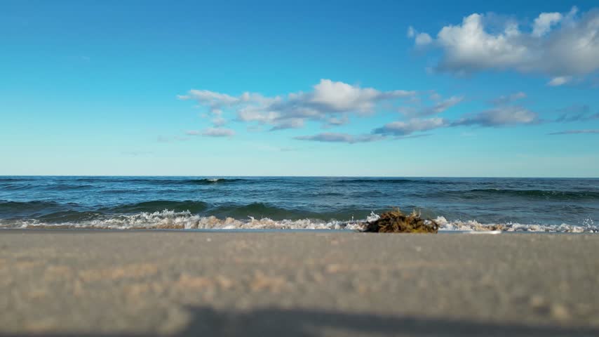 Gentle ocean waves roll onto a sandy shore on a sunny morning in the Magdalen Islands, Quebec, Canada.