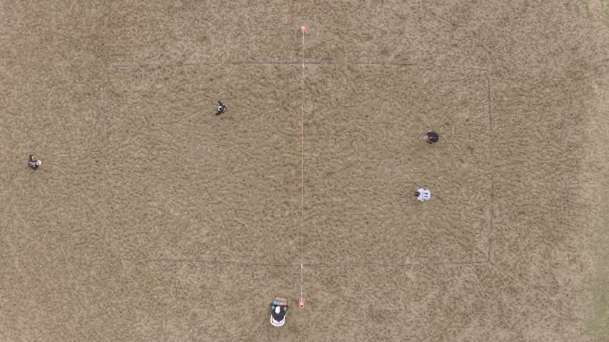 Top-down aerial shot of four athletes playing a competitive beach volleyball match on a sand court with a net and referee.