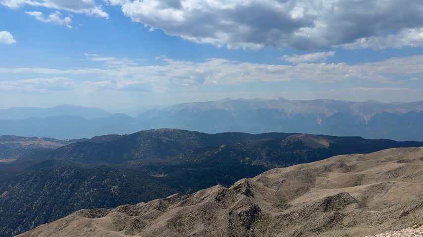 Expansive view of mountains and valleys under a clear sky, highlighting the rugged terrain and distant hills in a serene natural setting