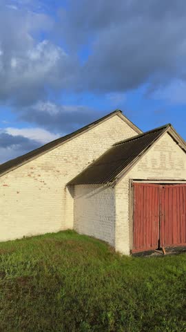 Traditional farming building with red doors and white brick exterior, set against a vibrant blue sky and lush green grass in a rural agricultural area