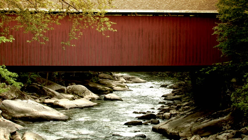 A red covered bridge over a flowing stream.