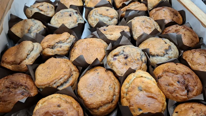 Large group of freshly baked blueberry muffins in brown paper liners close up, sweet traditional confectionery products at a bakery shop display concept.