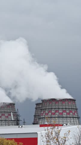 Thick white steam rising from the cooling towers of a thermal power station against a gray, overcast sky, representing industrial energy production and its environmental consequences