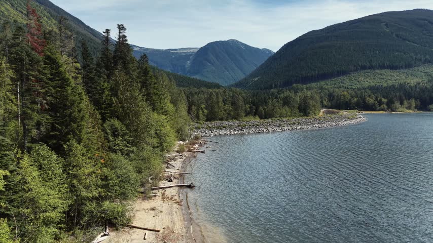 Drone shot of a riprap shoreline and access road along a mountain lake in British Columbia