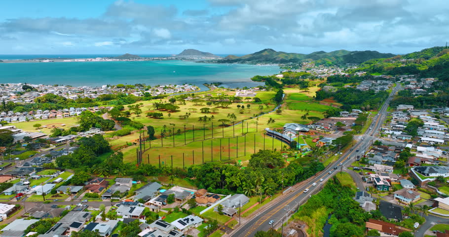 Approaching green golf course surrounded by urban landscape of Honolulu, Hawaii, USA. Azure waterscape of the Pacific Ocean at backdrop.